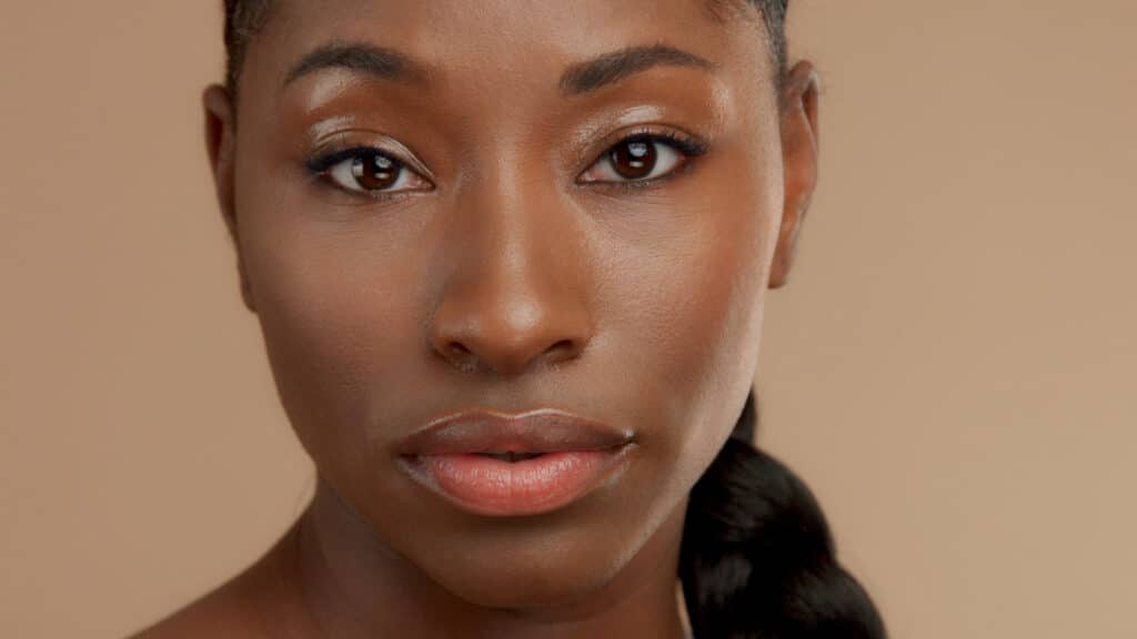 closeup portrait of mixed race black woman watching to the camera. Ideal skin, natural makeup, shiny glossy eyelids